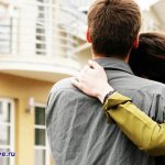 Молодая парочка, обнявшись, смотрит на желтый дом